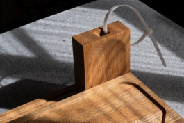 Close-up of BO cutting board by Simon Busse Studio for Collect, with cable tie and upright piece, on a textured gray surface in sunlight.