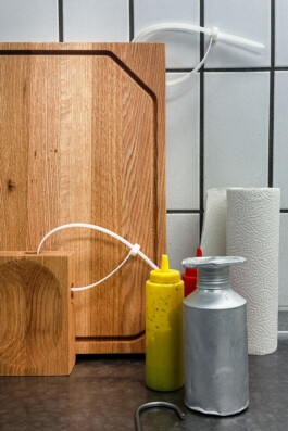 BO cutting boards by Simon Busse for Collect, with condiment bottles, metal container, paper towels, and a zip tie to hang the board. All on a silver stainless steel countertop. 