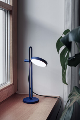 Minimalistische Designerlampe „Echo“ von Simon Busse in Blau, stehend auf Holzfensterbank. 