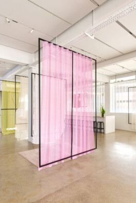 Simon Busse Studio portfolio: A contemporary open office space is defined by three sheer, pastel-coloured curtains—soft pink at the front and gentle yellow at the back—suspended from minimalist black metal frames, creating functional divisions within the workspace. The industrial design approach maximises natural light throughout the room, highlighting Simon Busse Studio’s focus on clarity and spatial organisation.